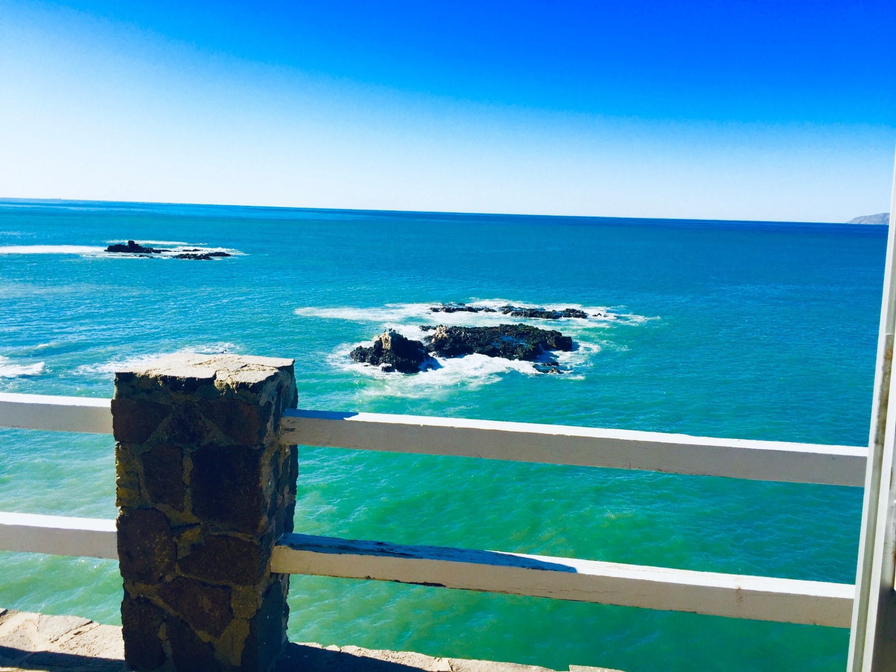 Turquoise Pacific water and rock outcrops seen over the property's stone-and-white railing